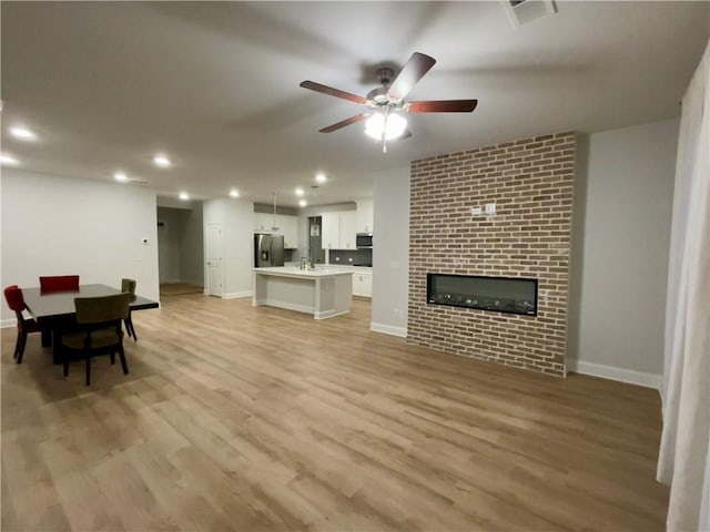 living room featuring ceiling fan, a large fireplace, sink, and light wood-type flooring