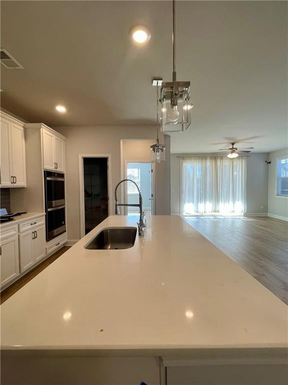 kitchen with sink, white cabinetry, double oven, decorative light fixtures, and a large island with sink