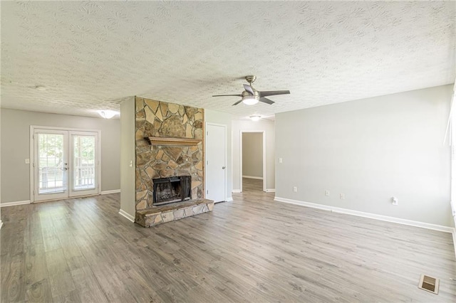 unfurnished living room with french doors, a textured ceiling, ceiling fan, wood-type flooring, and a stone fireplace