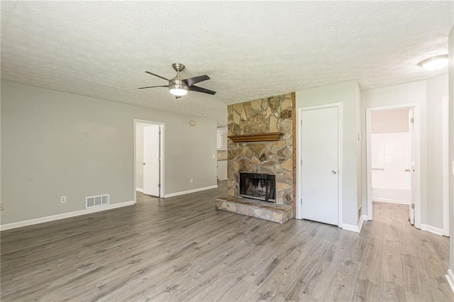 unfurnished living room featuring ceiling fan, a stone fireplace, wood-type flooring, and a textured ceiling