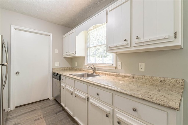 kitchen featuring light wood-type flooring, a textured ceiling, sink, dishwasher, and white cabinetry