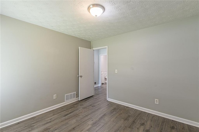 spare room featuring a textured ceiling and dark hardwood / wood-style flooring