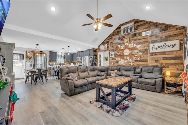 living room featuring light hardwood / wood-style floors, ceiling fan, wooden walls, and high vaulted ceiling