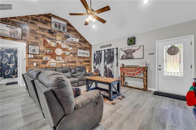 living room featuring high vaulted ceiling, light hardwood / wood-style flooring, wooden walls, and ceiling fan