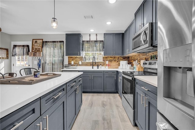 kitchen with stainless steel appliances, backsplash, light hardwood / wood-style flooring, gray cabinetry, and pendant lighting