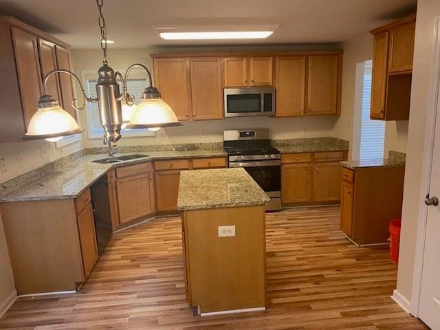 kitchen featuring decorative light fixtures, sink, a center island, stainless steel appliances, and light wood-type flooring