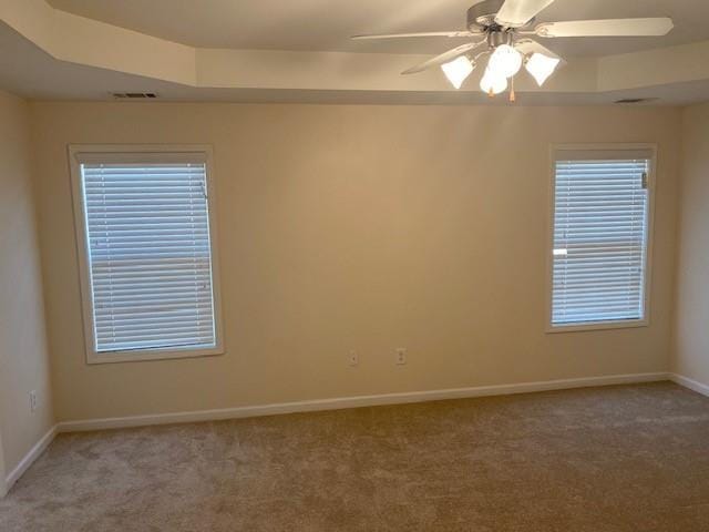 carpeted spare room featuring ceiling fan and a raised ceiling