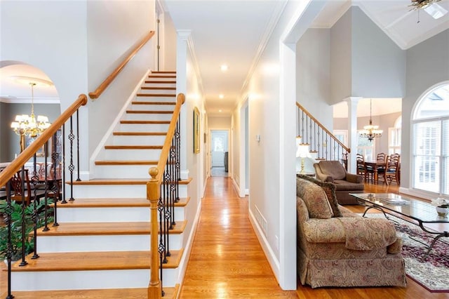 staircase with arched walkways, an inviting chandelier, wood finished floors, and ornamental molding