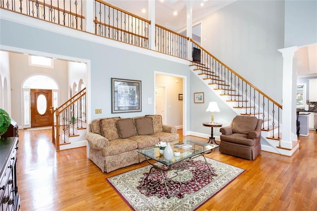 living room with stairway, a high ceiling, wood finished floors, and ornate columns