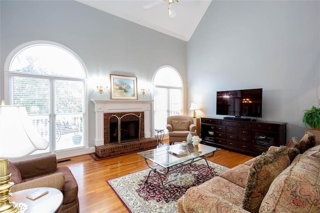 living room with visible vents, a brick fireplace, ceiling fan, wood finished floors, and high vaulted ceiling