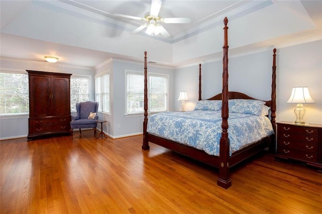 bedroom with a tray ceiling, crown molding, multiple windows, and wood finished floors