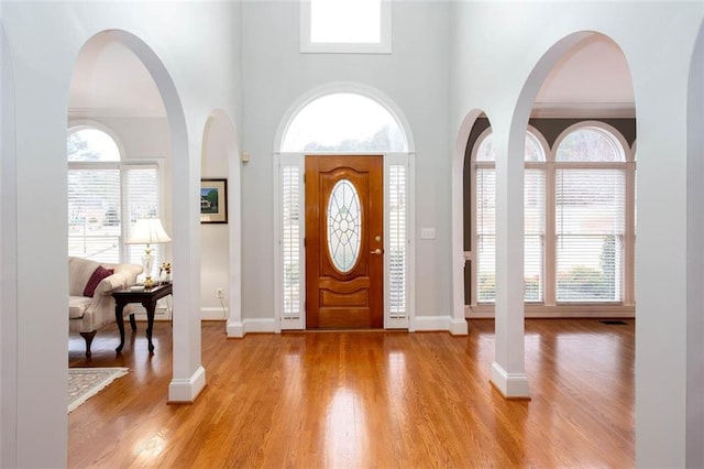 foyer entrance with baseboards, light wood-style flooring, and a towering ceiling