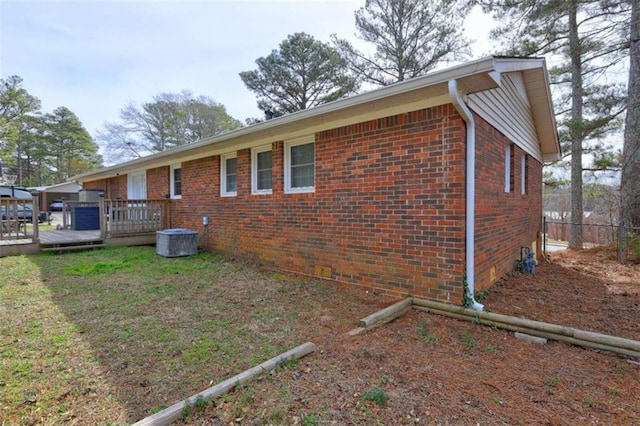 view of side of property with central AC unit, brick siding, fence, a lawn, and a wooden deck