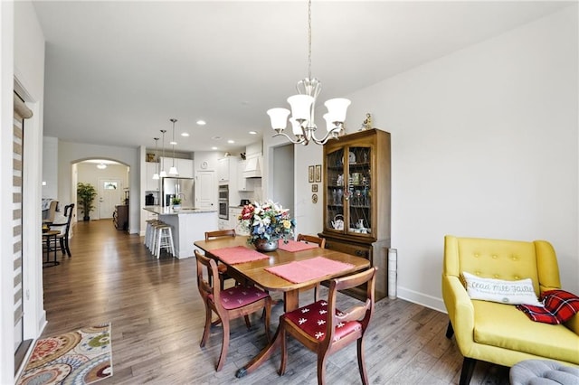 dining space featuring arched walkways, dark wood-style flooring, a chandelier, baseboards, and recessed lighting