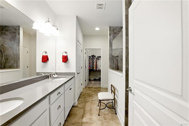 bathroom with double vanity, a walk in closet, a tile shower, recessed lighting, and baseboards