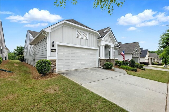 view of front of property with board and batten siding, a garage, stone siding, driveway, and a front yard