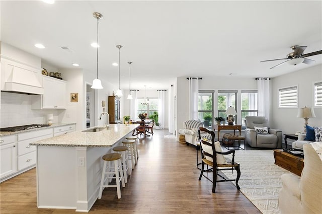 kitchen with a sink, gas cooktop, open floor plan, wood finished floors, and a center island with sink