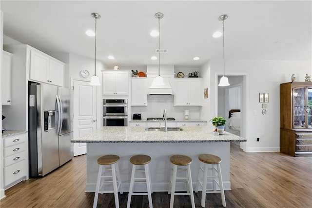 kitchen with stainless steel appliances, premium range hood, wood finished floors, white cabinetry, and recessed lighting