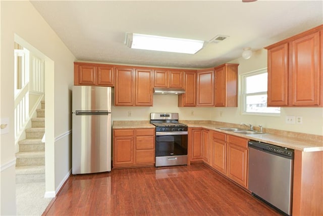 kitchen featuring dark wood-style flooring, light countertops, appliances with stainless steel finishes, a sink, and under cabinet range hood