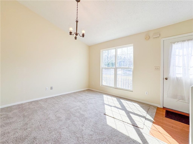 carpeted empty room featuring a chandelier, a wealth of natural light, vaulted ceiling, and a textured ceiling