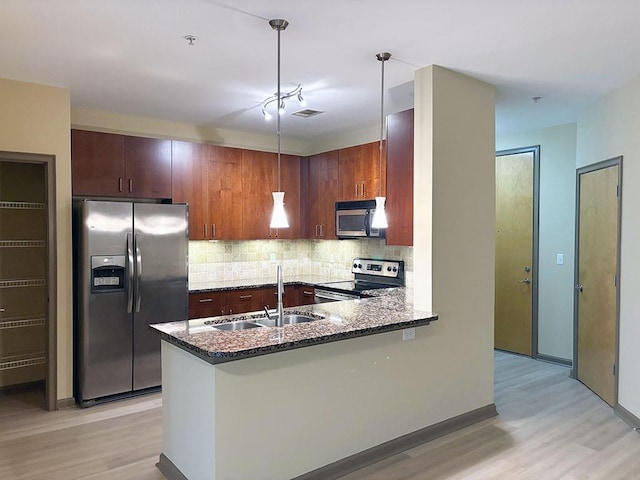 kitchen with sink, kitchen peninsula, decorative light fixtures, appliances with stainless steel finishes, and light wood-type flooring