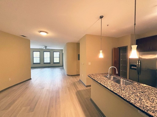 kitchen with stainless steel refrigerator with ice dispenser, dark stone counters, sink, pendant lighting, and hardwood / wood-style floors