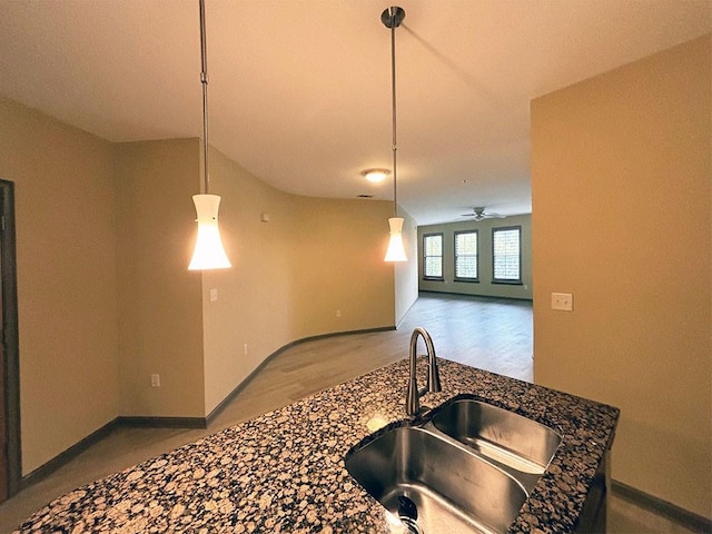 kitchen with ceiling fan, sink, dark stone countertops, pendant lighting, and light hardwood / wood-style floors