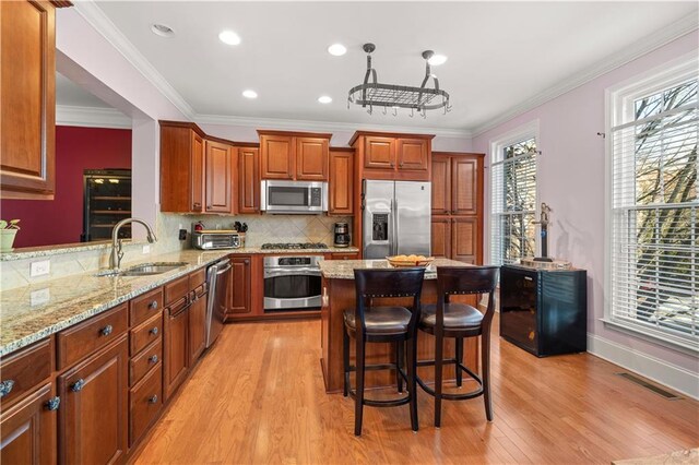 kitchen with appliances with stainless steel finishes, hanging light fixtures, light wood-type flooring, and tasteful backsplash