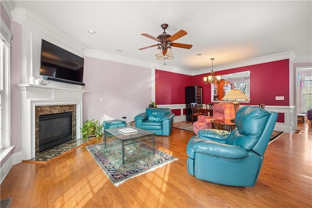 living room with ceiling fan with notable chandelier, a high end fireplace, ornamental molding, and hardwood / wood-style flooring