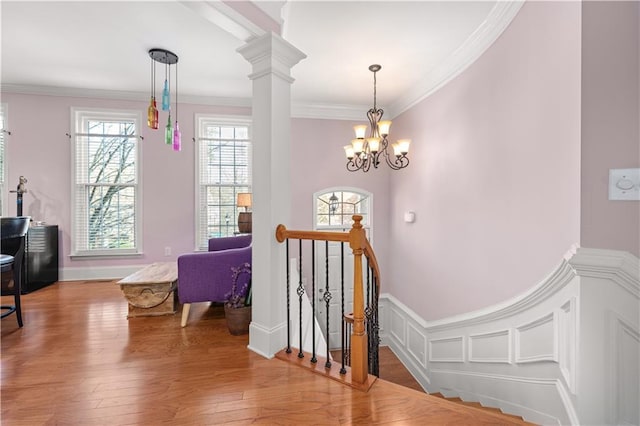 stairs featuring ornate columns, wood-type flooring, ornamental molding, and a notable chandelier