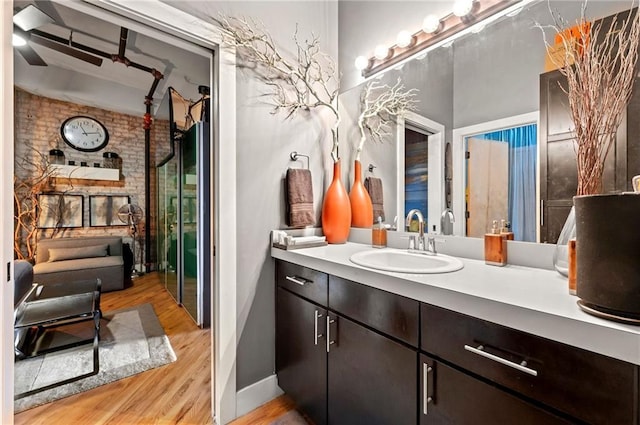 bathroom featuring vanity, wood finished floors, baseboards, and brick wall