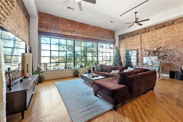 living room with a ceiling fan, wood finished floors, visible vents, and brick wall