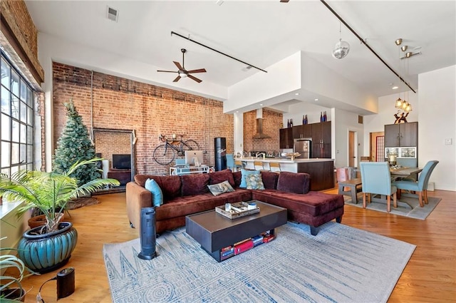 living area with visible vents, light wood-style flooring, brick wall, and ceiling fan