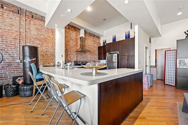 kitchen with light wood-style flooring, wall chimney range hood, appliances with stainless steel finishes, brick wall, and light countertops