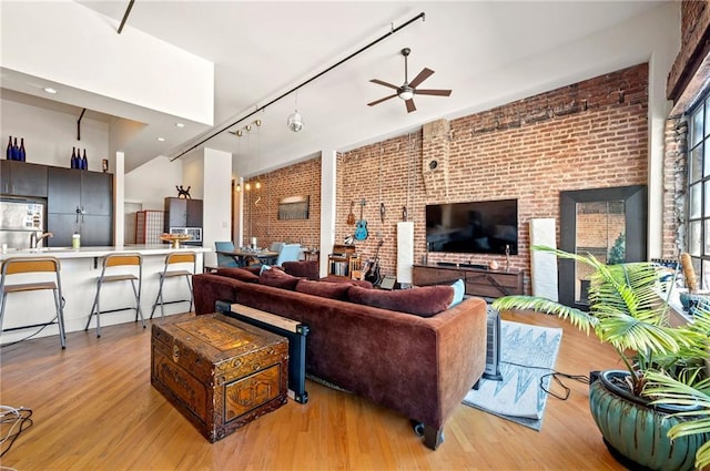 living room with light wood finished floors, brick wall, rail lighting, and a ceiling fan