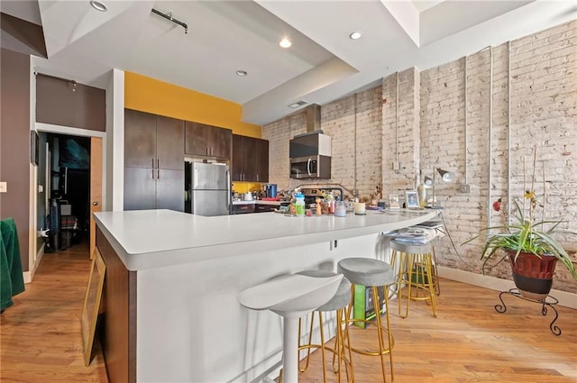 kitchen with light countertops, light wood-style flooring, brick wall, and stainless steel appliances