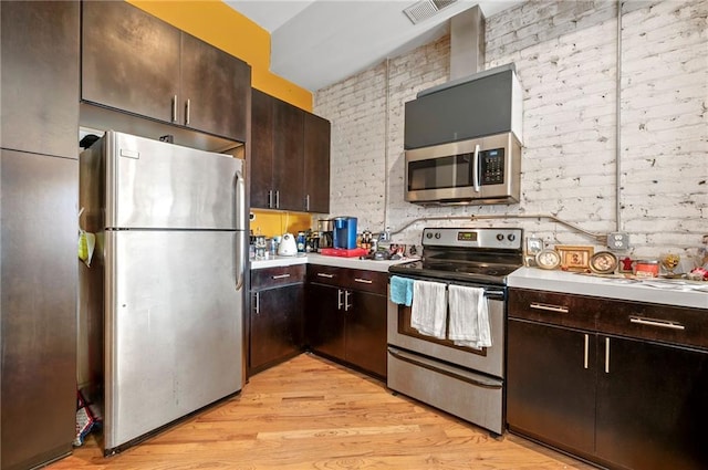 kitchen featuring visible vents, brick wall, light countertops, light wood-style floors, and stainless steel appliances