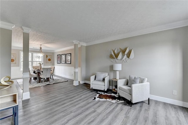 living area with hardwood / wood-style floors, crown molding, a textured ceiling, and ornate columns