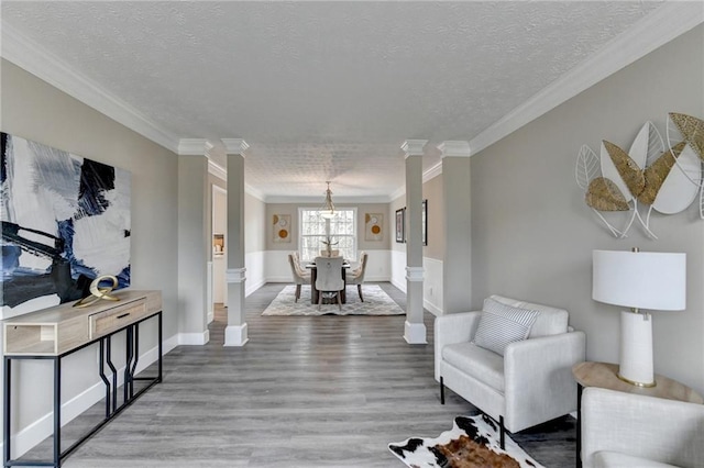 living room featuring hardwood / wood-style flooring, ornamental molding, decorative columns, and a textured ceiling