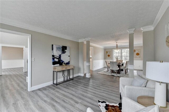 living room featuring crown molding, hardwood / wood-style flooring, a textured ceiling, and ornate columns