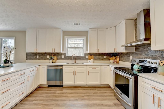 kitchen with sink, wall chimney range hood, stainless steel appliances, light hardwood / wood-style floors, and white cabinets