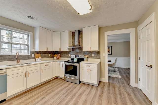 kitchen with sink, appliances with stainless steel finishes, white cabinets, wall chimney exhaust hood, and light wood-type flooring