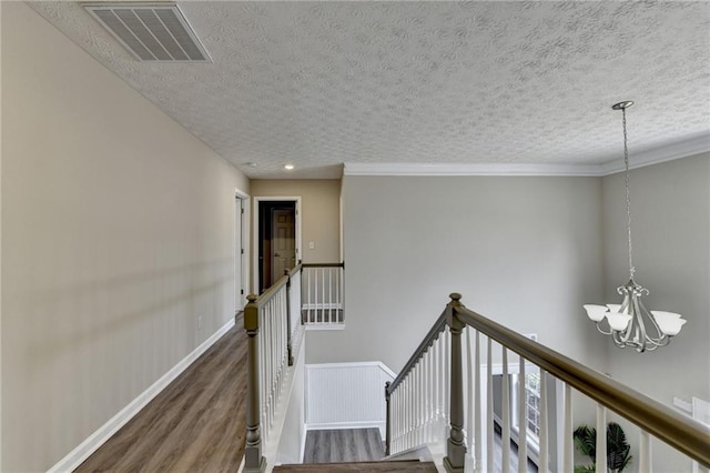 stairs with hardwood / wood-style flooring, crown molding, a textured ceiling, and an inviting chandelier