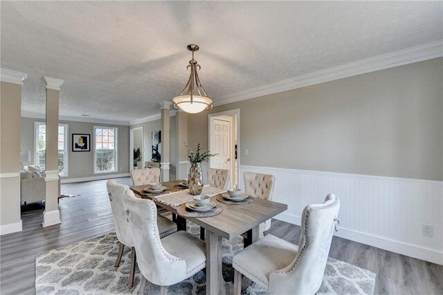 dining space with dark wood-type flooring, crown molding, and decorative columns