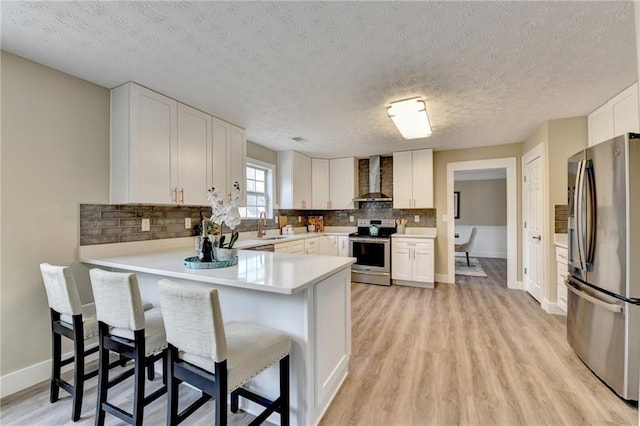 kitchen with appliances with stainless steel finishes, white cabinetry, a breakfast bar area, kitchen peninsula, and wall chimney range hood