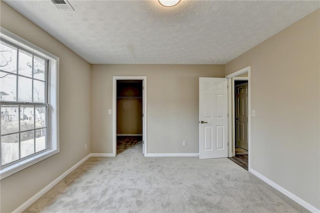 unfurnished bedroom with multiple windows, a walk in closet, light carpet, and a textured ceiling