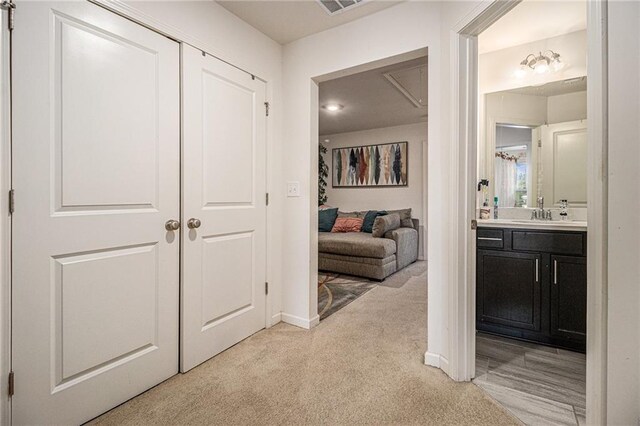 hall with baseboards, visible vents, light carpet, and a sink