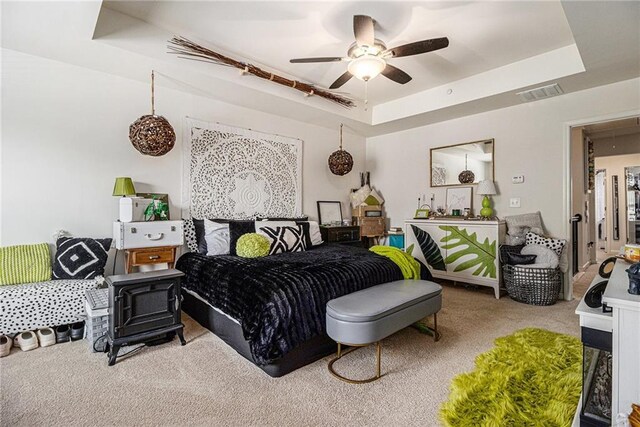carpeted bedroom featuring a ceiling fan, a tray ceiling, and visible vents