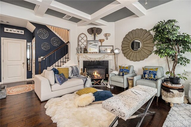 living area featuring wood-type flooring, a glass covered fireplace, stairs, beamed ceiling, and coffered ceiling