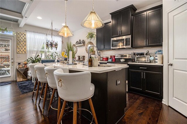 kitchen with light countertops, appliances with stainless steel finishes, a center island with sink, and dark wood-style flooring